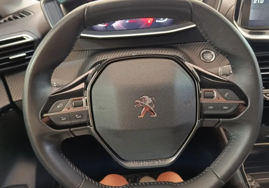 Vue rapprochée du volant cuir noir de la Peugeot 208 blanc, avec commandes intégrées et bouton démarrage visible.