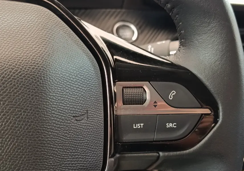 Gros plan sur les commandes gauche du volant cuir noir du Peugeot 208 blanc, avec bouton appel et molette de réglage.