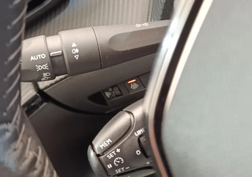 Gros plan sur commandes au volant et commodo d’éclairage d’une Peugeot 208 blanche, version PureTech 100 S&S Allure Business.