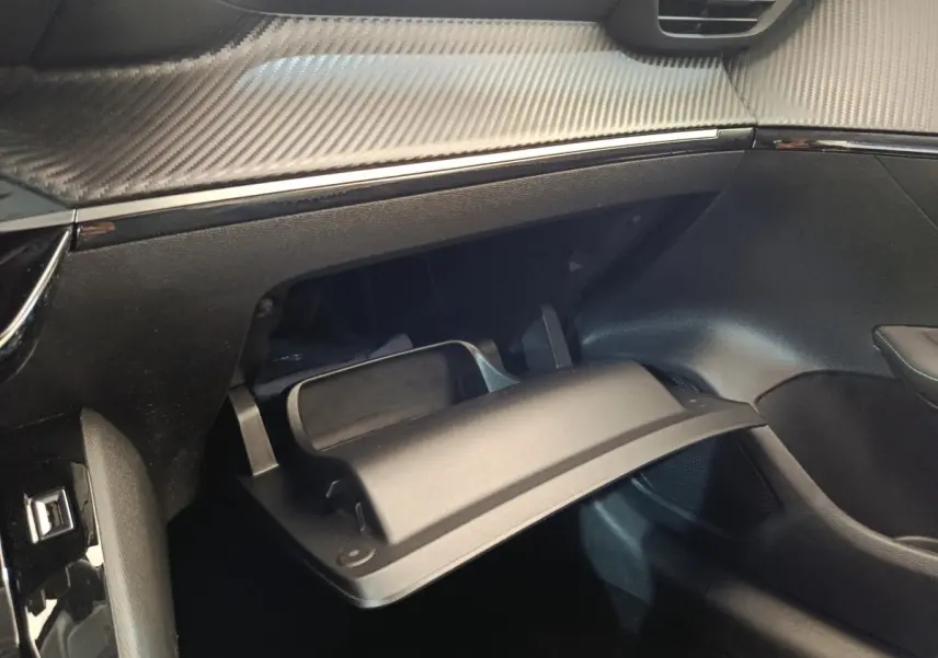 Vue intérieure côté passager du coffre à gants ouvert avec tableau de bord noir et finition effet carbone sur Peugeot 208 blanc.