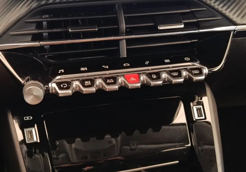 Vue rapprochée de la console centrale noire brillante de la Peugeot 208 PureTech 100 avec boutons de commande et ports USB.