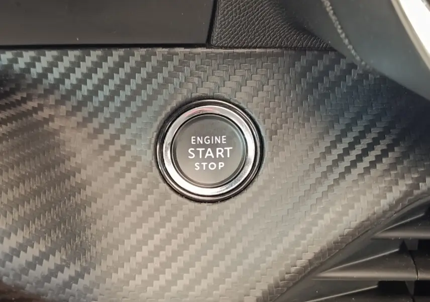 Gros plan sur le bouton start/stop entouré d'un décor noir effet carbone dans l'habitacle d'une Peugeot 208 blanche.