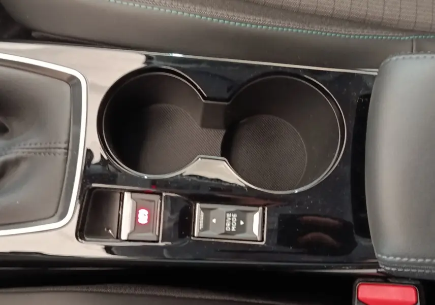 Gros plan sur la console centrale noire du Peugeot 208 blanc, montrant porte-gobelets et commandes mode de conduite et frein électrique.