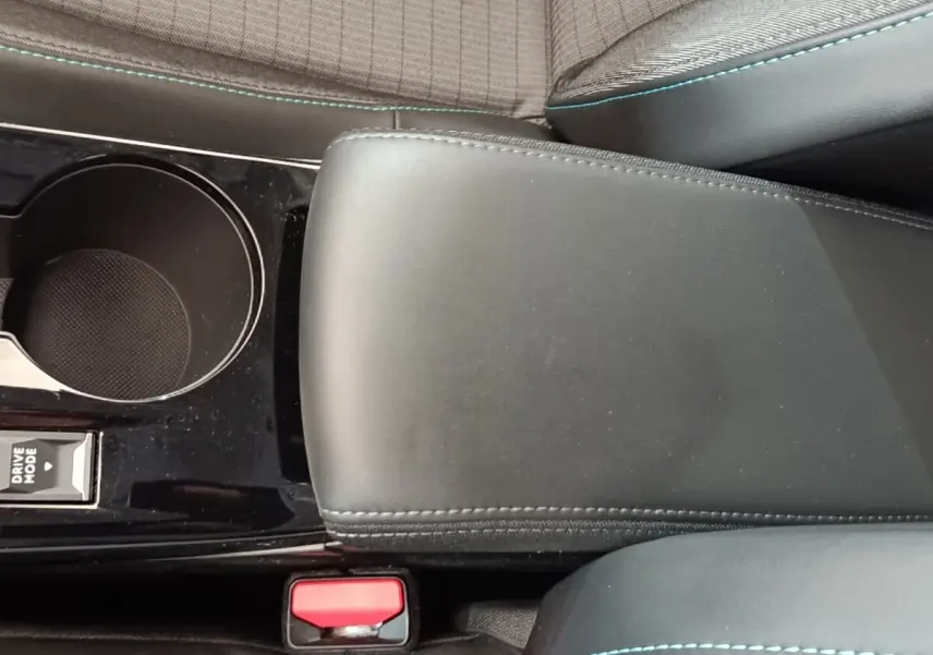 Gros plan sur l'accoudoir central noir et la console avec porte-gobelet de la Peugeot 208 PureTech 100 blanche.