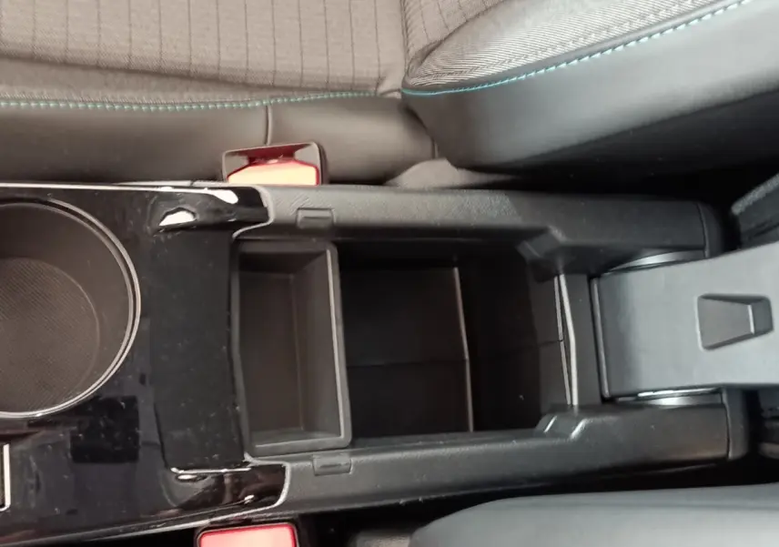 Vue plongeante sur la console centrale noire de la Peugeot 208 blanche, avec porte-gobelets et accoudoir ouvert.