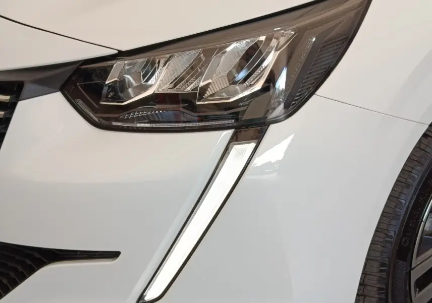 Gros plan sur le phare avant droit LED et la carrosserie blanche d'une Peugeot 208 PureTech 100 S&S Allure Business.