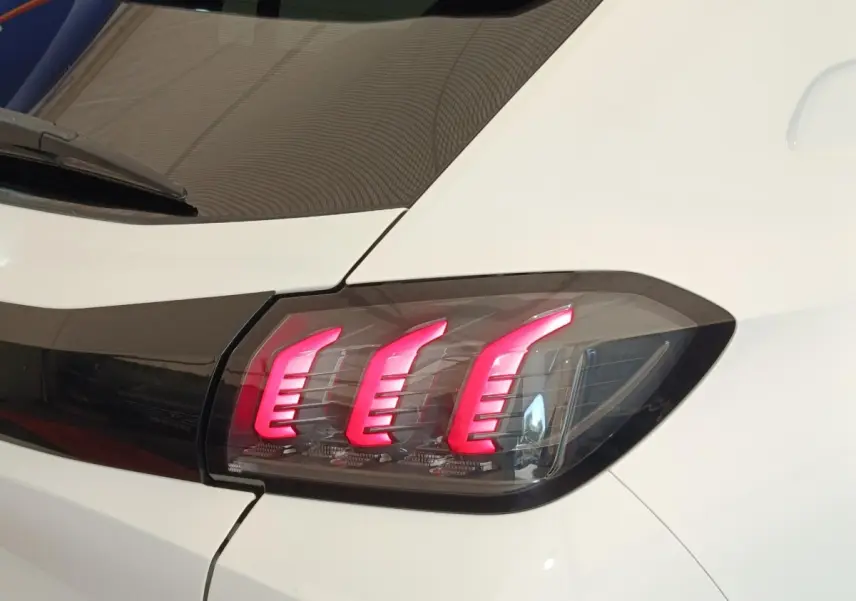 Gros plan sur le feu arrière droit allumé d’une Peugeot 208 blanche, soulignant ses trois griffes lumineuses rouges.
