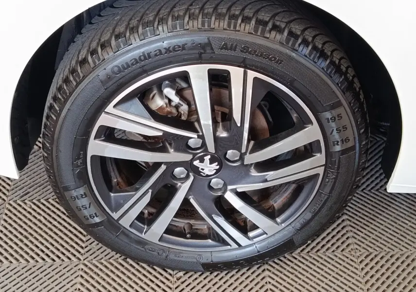 Gros plan sur la roue avant droite d'une Peugeot 208 blanche avec jante alliage noire et argentée.
