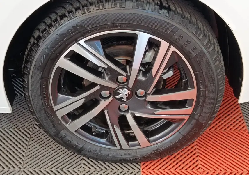 Gros plan sur la jante alliage bicolore avec logo Peugeot, roue avant droite d'une Peugeot 208 blanche.