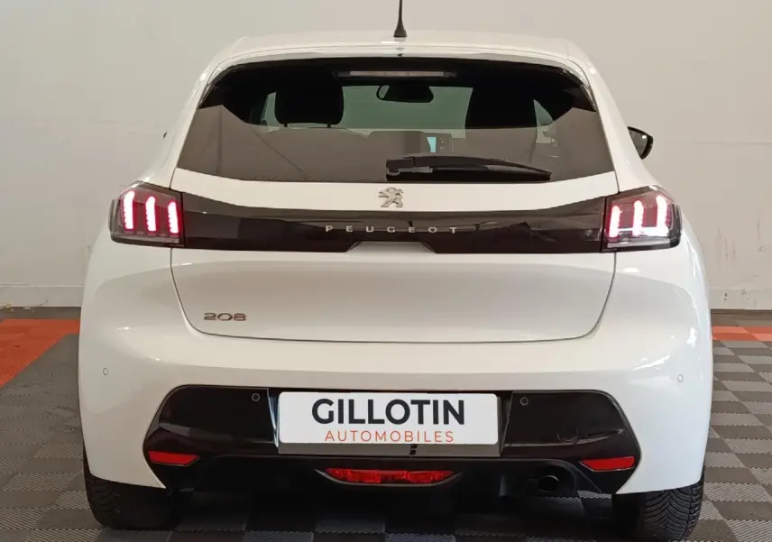 Vue arrière d'une Peugeot 208 blanche de 2021 avec feux LED allumés et logo Peugeot visible sur hayon noir.