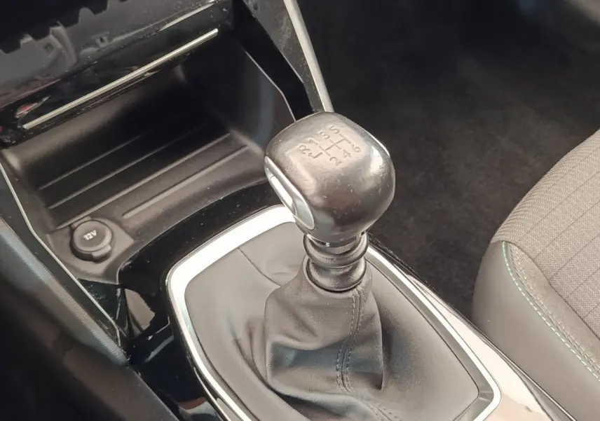 Gros plan sur le levier de vitesses manuel noir et console centrale brillante dans l’habitacle d’une Peugeot 208 blanche.