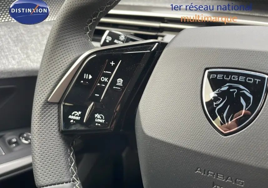 Gros plan sur le volant en cuir perforé du Peugeot 5008 gris, avec commandes intégrées et logo lion central.