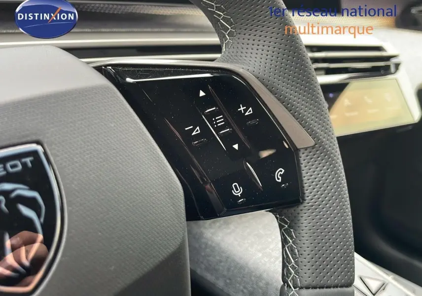 Gros plan sur le volant en cuir perforé gris du Peugeot 5008 Hybrid 2025 avec commandes audio intégrées.