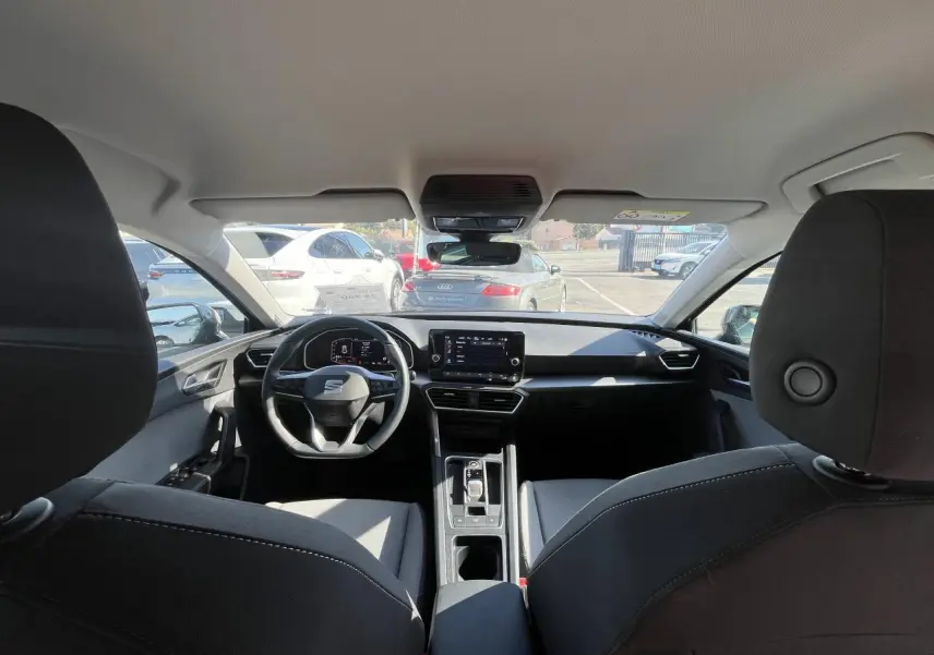 Vue intérieure avant du SEAT Leon IV gris, mettant en valeur le volant cuir multifonction et l'écran digital central.