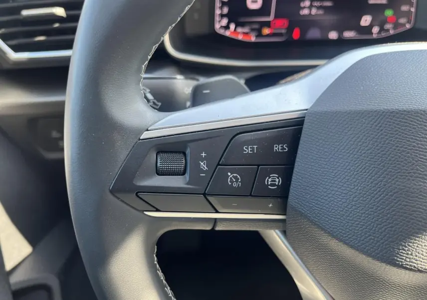 Gros plan sur les commandes du volant cuir multifonction du SEAT Leon IV gris Magnetic Metal, affichage numérique en arrière-plan.