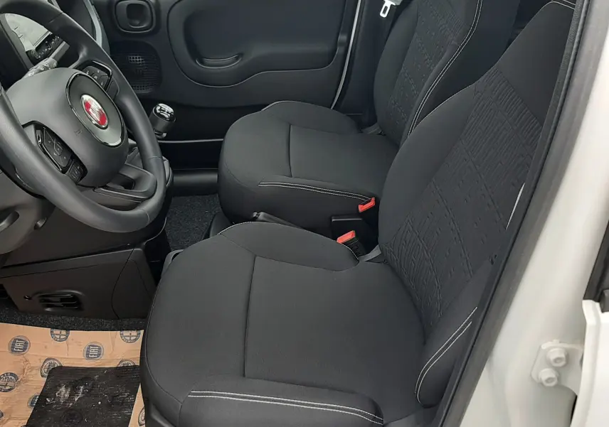 Vue intérieure côté conducteur de la Fiat Panda blanc gelato 2025, sièges noirs en tissu et volant multifonction.