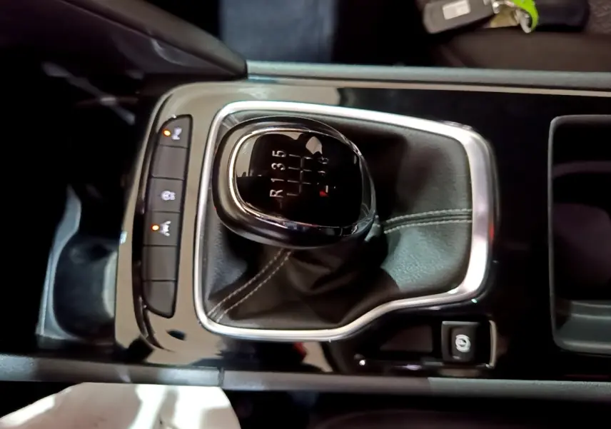 Gros plan sur levier de vitesses manuel noir avec coutures blanches dans console centrale brillante d’Opel Insignia rouge.