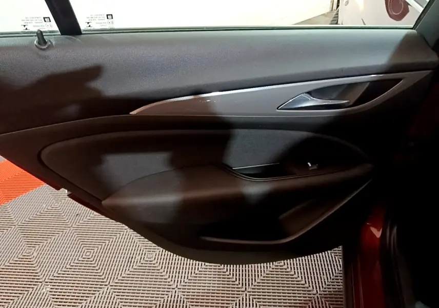 Vue intérieure de la porte arrière droite noire de l’Opel Insignia rouge, avec poignée argentée et bouton de lève-vitre.