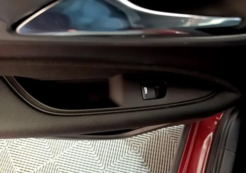 Gros plan sur la poignée intérieure et la commande de verrouillage de la porte côté gauche d’une Opel Insignia rouge.