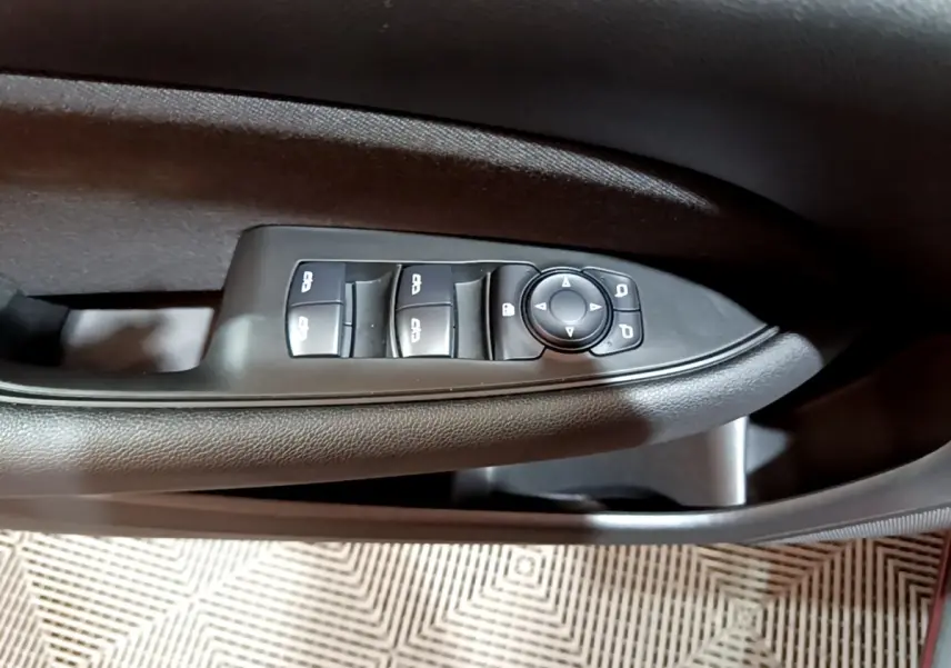 Gros plan sur les commandes des vitres et rétroviseurs côté gauche de la porte intérieure noire d’une Opel Insignia rouge.
