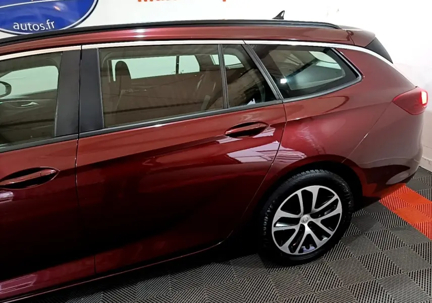 Vue latérale côté droit d'une Opel Insignia break rouge métallisé, mettant en valeur la roue arrière et les vitres teintées.