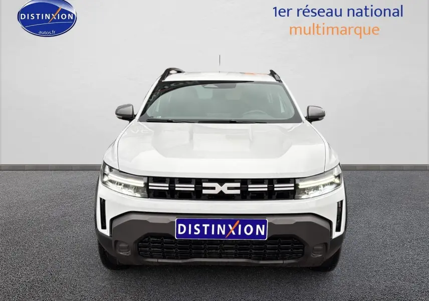 Vue avant du Dacia Duster blanc arctic avec calandre noire et phares LED allumés sur fond neutre.