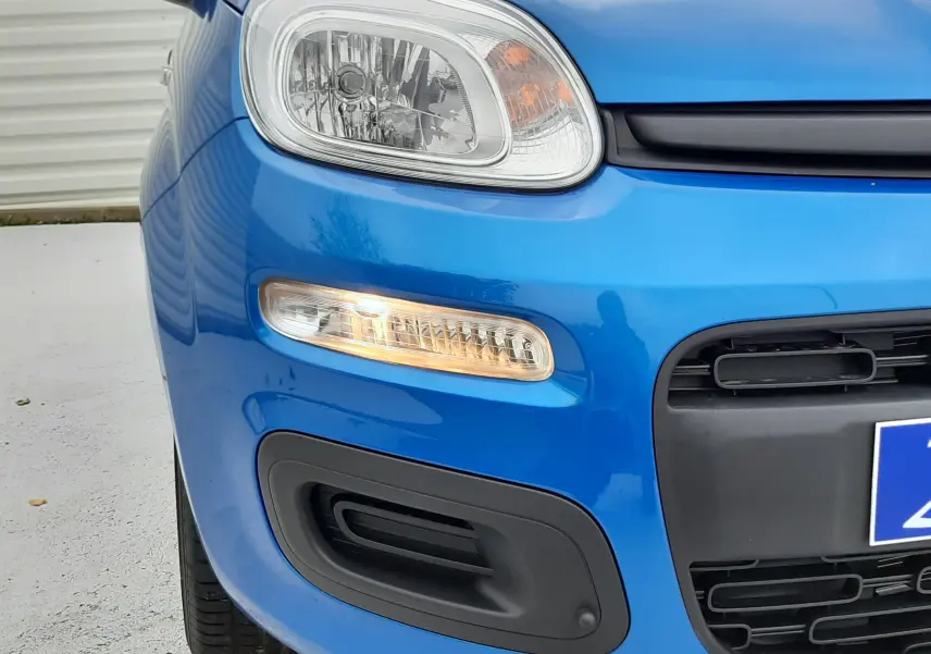 Vue 3/4 avant gauche d'une Fiat Panda 2025 bleu Italia avec éclairage allumé et pare-chocs noir mat distinctif.