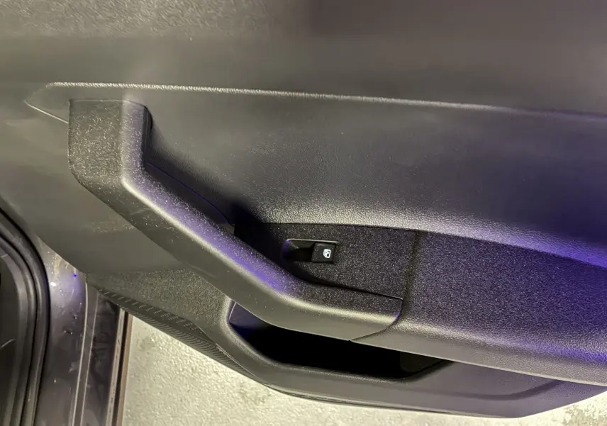 Poignée intérieure côté gauche de la porte d’une Volkswagen Polo gris 2025 avec bouton de commande de vitre électrique.