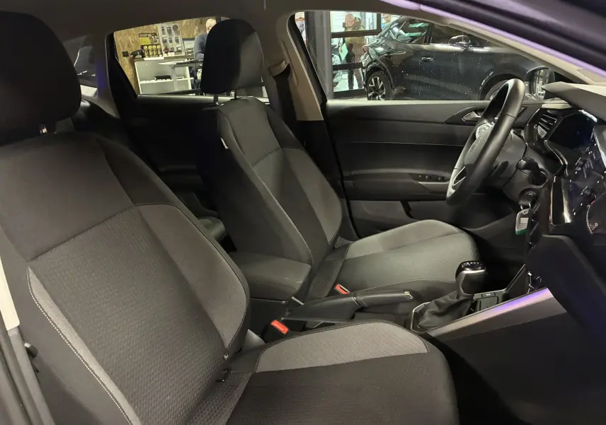 Vue intérieure côté conducteur de la Volkswagen Polo gris 2025, sièges tissu noir et console centrale avec boîte auto.