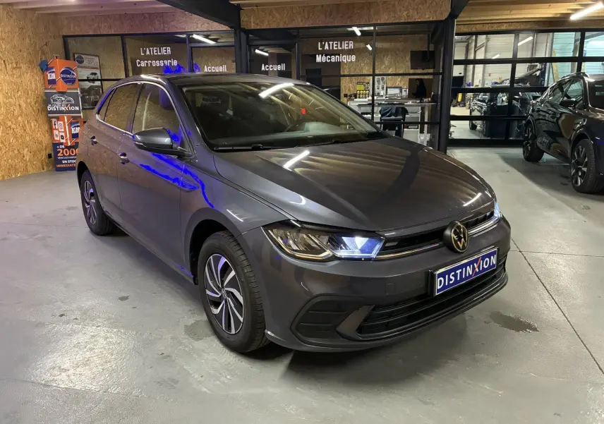 Volkswagen Polo VI gris vue 3/4 avant droit avec phares allumés, stationnée en intérieur dans un garage.