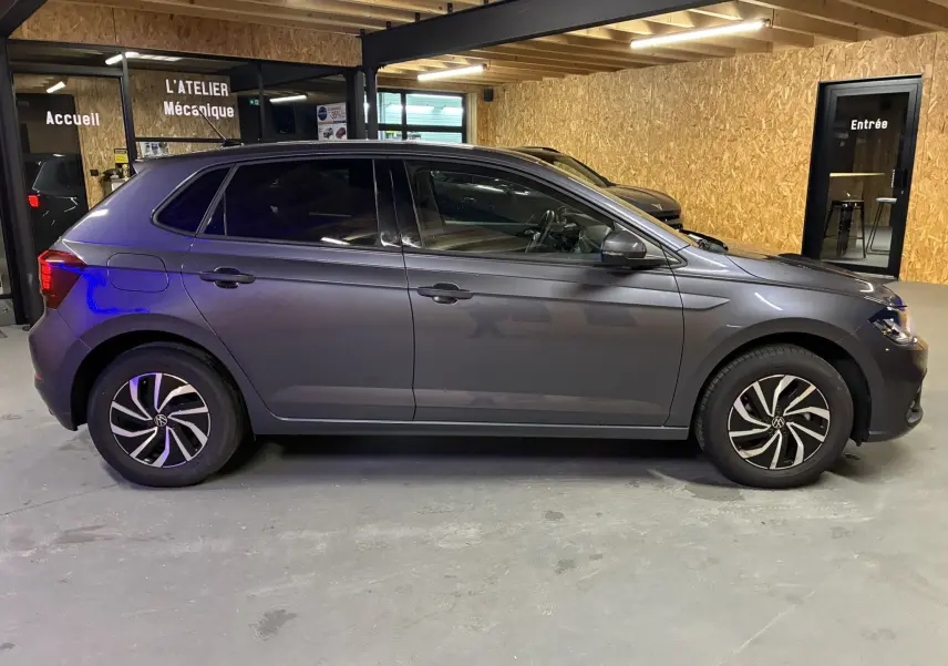 Profil côté gauche d'une Volkswagen Polo gris métallisé 2025 en intérieur, avec jantes bi-ton et vitres teintées.