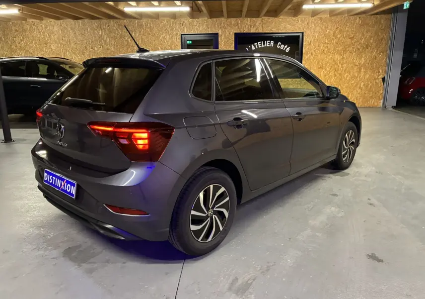 Volkswagen Polo gris vue 3/4 arrière droit en intérieur avec feux arrière allumés et jantes bi-ton.