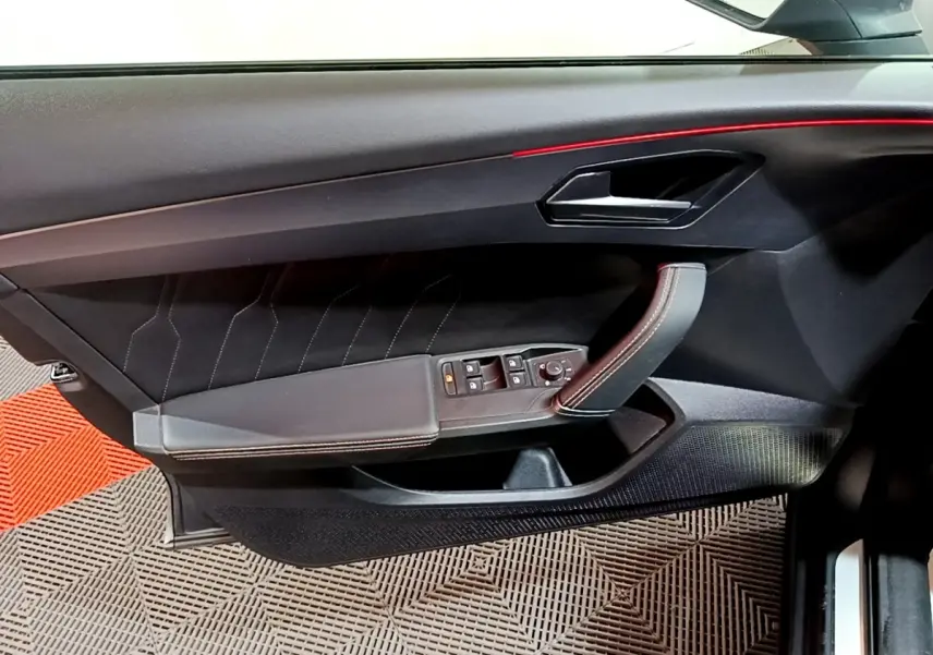 Vue intérieure du panneau de porte côté gauche de la CUPRA Formentor gris foncé, avec commandes électriques et surpiqûres rouges.