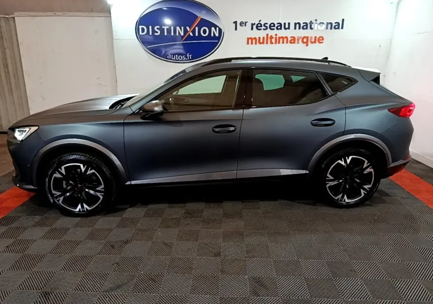 Vue de profil côté gauche d’un CUPRA Formentor gris foncé 2024 avec jantes noires à motifs blancs dans un showroom.