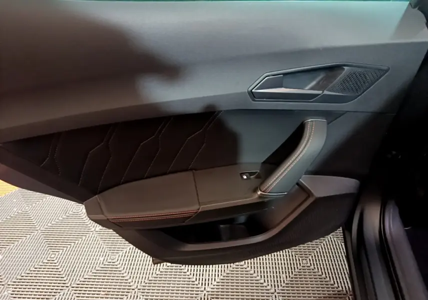 Vue intérieure côté gauche de la porte avant d'une CUPRA Formentor gris foncé avec surpiqûres rouges et poignée en cuir.
