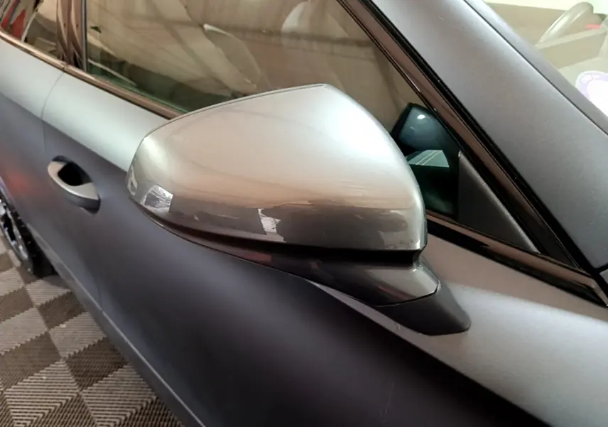 Gros plan sur le rétroviseur côté gauche d’un CUPRA Formentor gris foncé avec porte et vitre partiellement visibles.