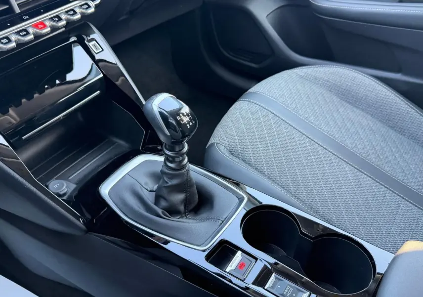 Vue rapprochée de la console centrale de la Peugeot 208 2025, avec levier de vitesse manuel et siège tissu gris.