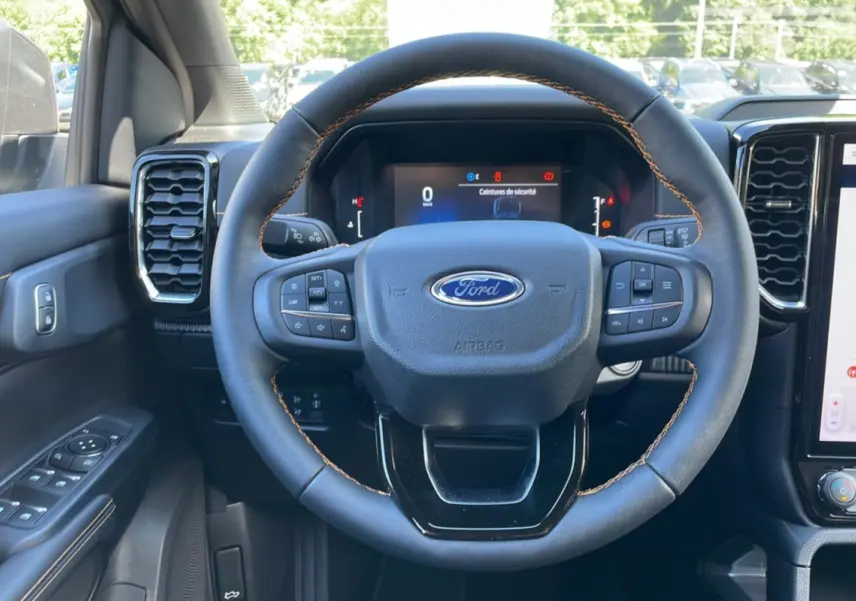 Vue rapprochée du volant cuir multifonctions du Ford Ranger gris carbone, avec tableau de bord numérique et commandes intégrées.