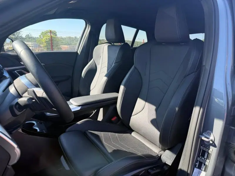 Vue intérieure côté conducteur de la BMW X2 2025, sièges sport en cuir noir avec accoudoir central et volant multifonction.