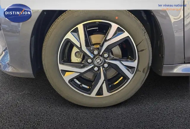 Gros plan sur la roue avant droite d'une Toyota Yaris hybride gris foncé, avec jante alliage au design moderne.