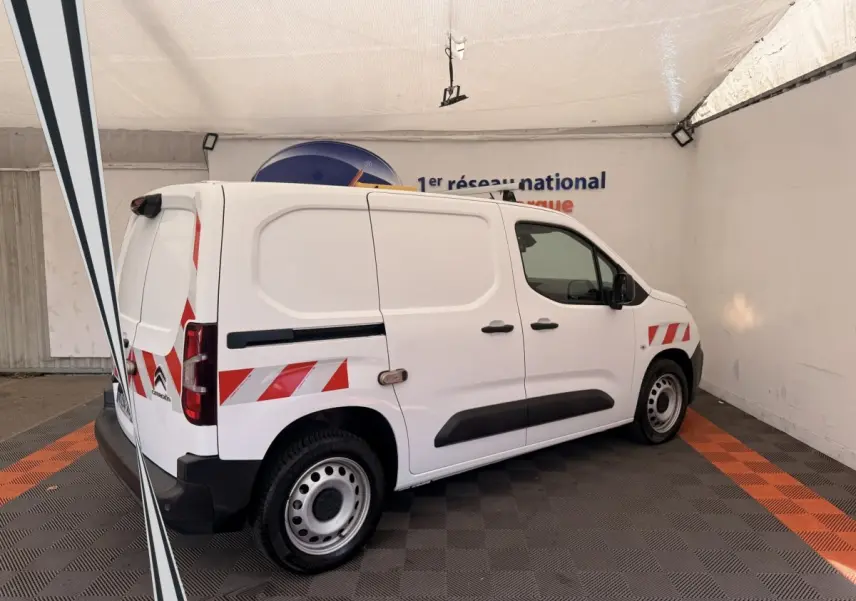 Vue de côté droit arrière d’un Citroën Berlingo blanc avec bandes réfléchissantes rouges et blanches sur la carrosserie.