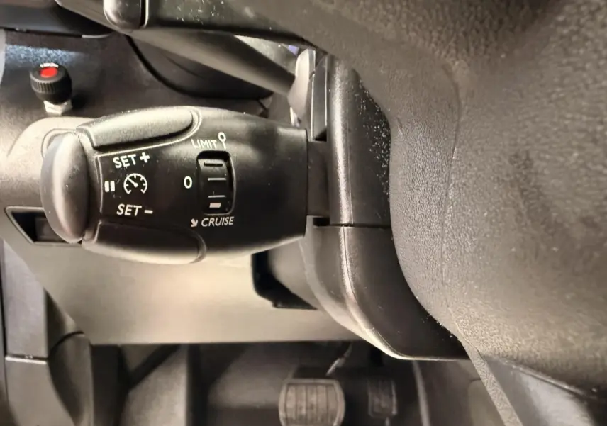 Gros plan sur la commande de régulateur de vitesse à gauche du volant dans l'habitacle du Citroën Berlingo blanc.
