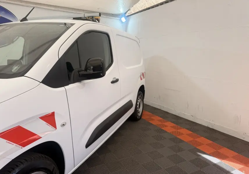 Vue de profil côté gauche d’un Citroën Berlingo blanc avec marquages rouges et protections noires sur porte.