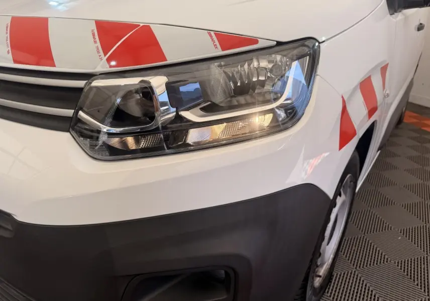 Gros plan sur l'avant droit blanc d'un Citroën Berlingo 2022 avec phare allumé et marquages rouges réfléchissants.