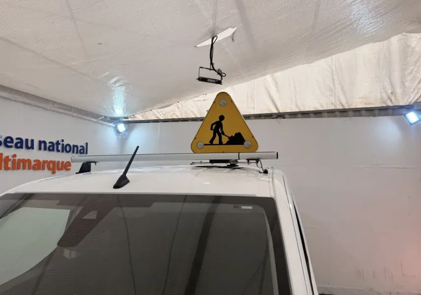 Vue avant rapprochée du toit blanc d’un Citroën Berlingo avec panneau triangulaire de chantier fixé dessus.