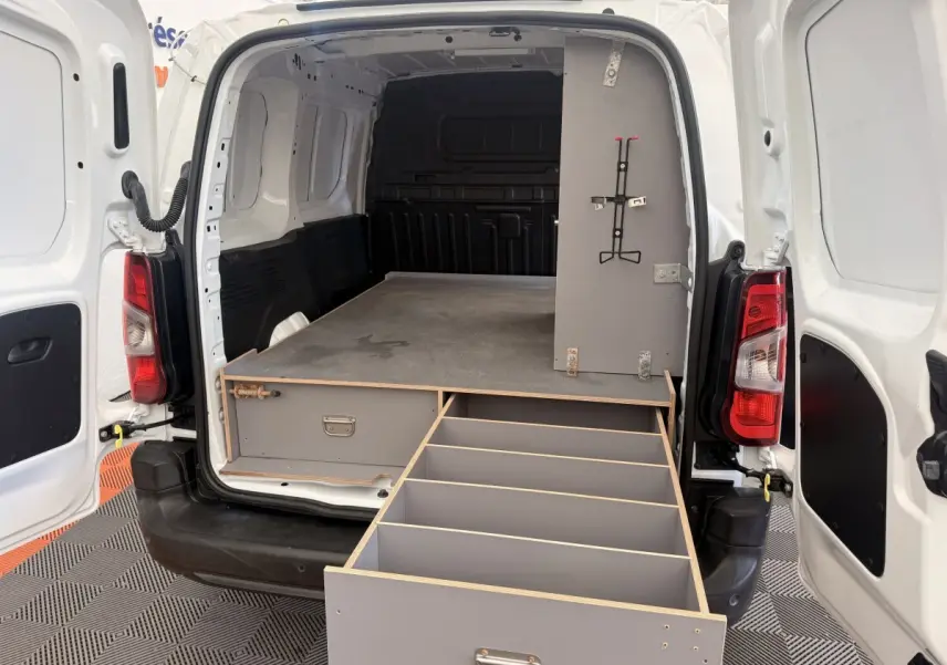 Vue arrière du Citroën Berlingo blanc avec portes ouvertes et tiroir de rangement gris déployé dans l’espace de chargement.