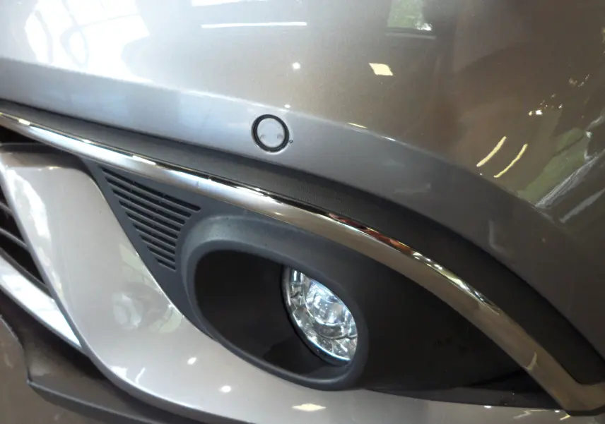 Gros plan sur le feu antibrouillard avant droit du Renault Grand Scenic IV gris Cassiopé avec détails chromés.