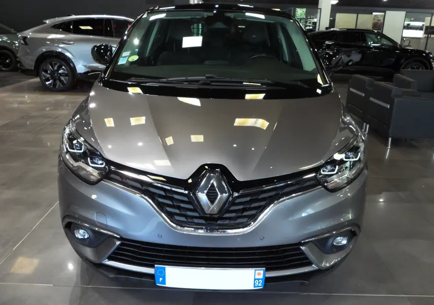 Vue avant d'un Renault Grand Scenic IV gris Cassiopé avec toit noir, mettant en valeur sa calandre et ses phares LED distinctifs.