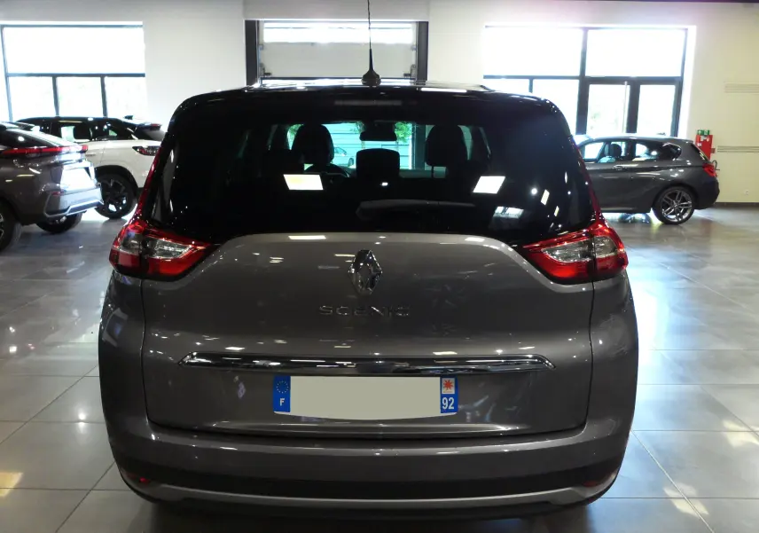 Vue arrière d'un Renault Grand Scenic IV gris Cassiopé avec toit noir, dans un showroom lumineux.