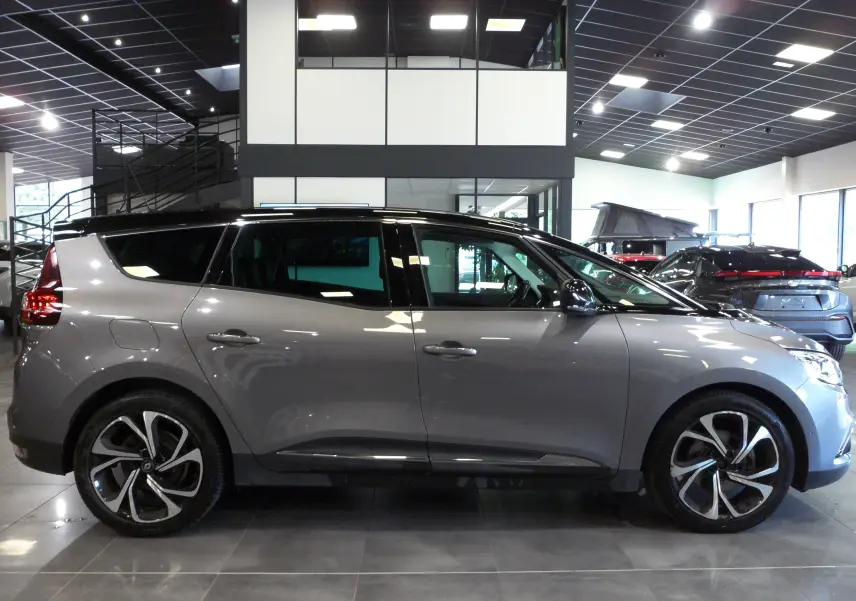 Profil droit du Renault Grand Scenic IV gris Cassiopé avec toit noir, jantes alliage et intérieur visible en showroom.